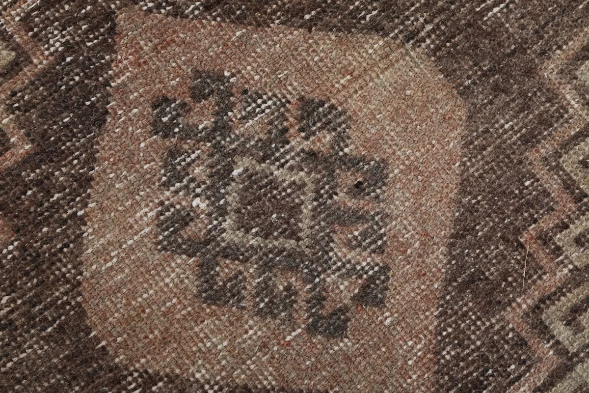Extreme close-up of the distressed brown geometric pattern within a diamond shape on the tan runner rug.