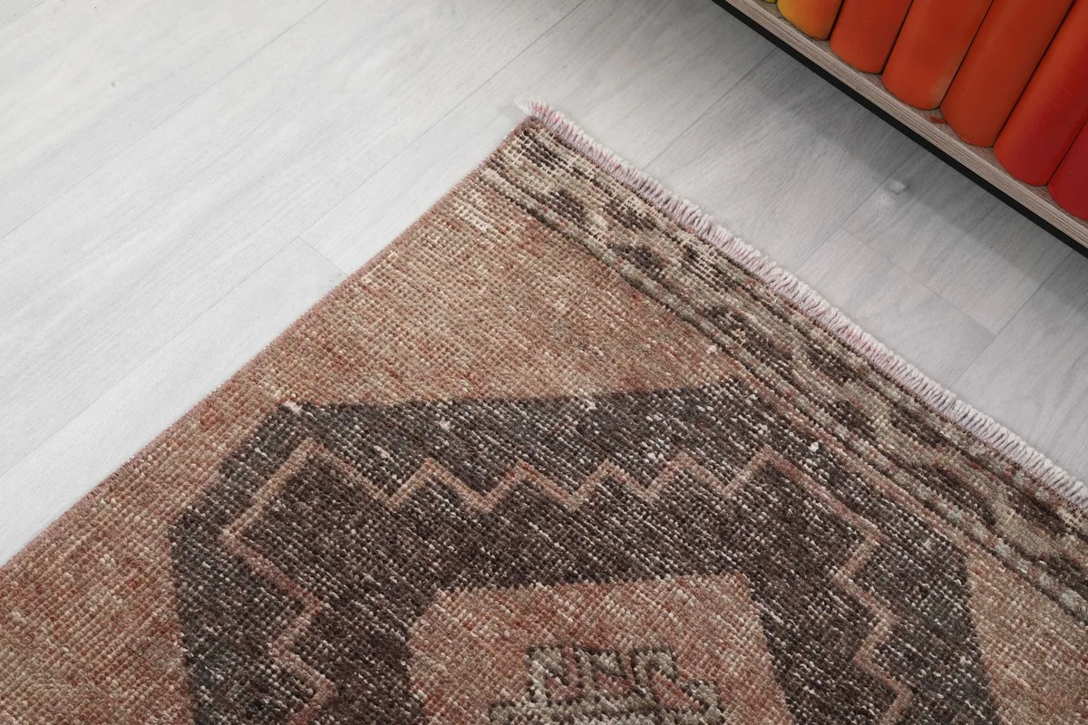 Close-up of the end border and corner of the tan runner rug, showing the geometric design and fringe.