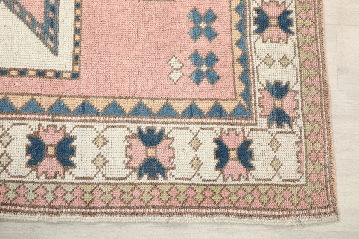 Detail of the corner border of the rose rug, showing blue and ivory tribal motifs.