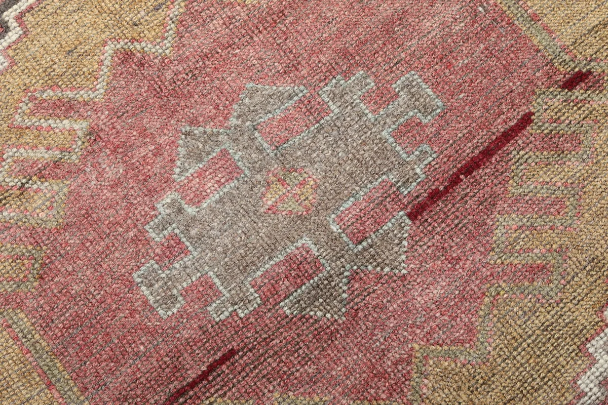 Close-up of a tribal geometric motif in gray and rose within a tan medallion