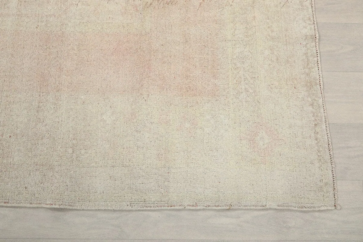 Detail of the rug's edge and subtle geometric patterns in cream and rose