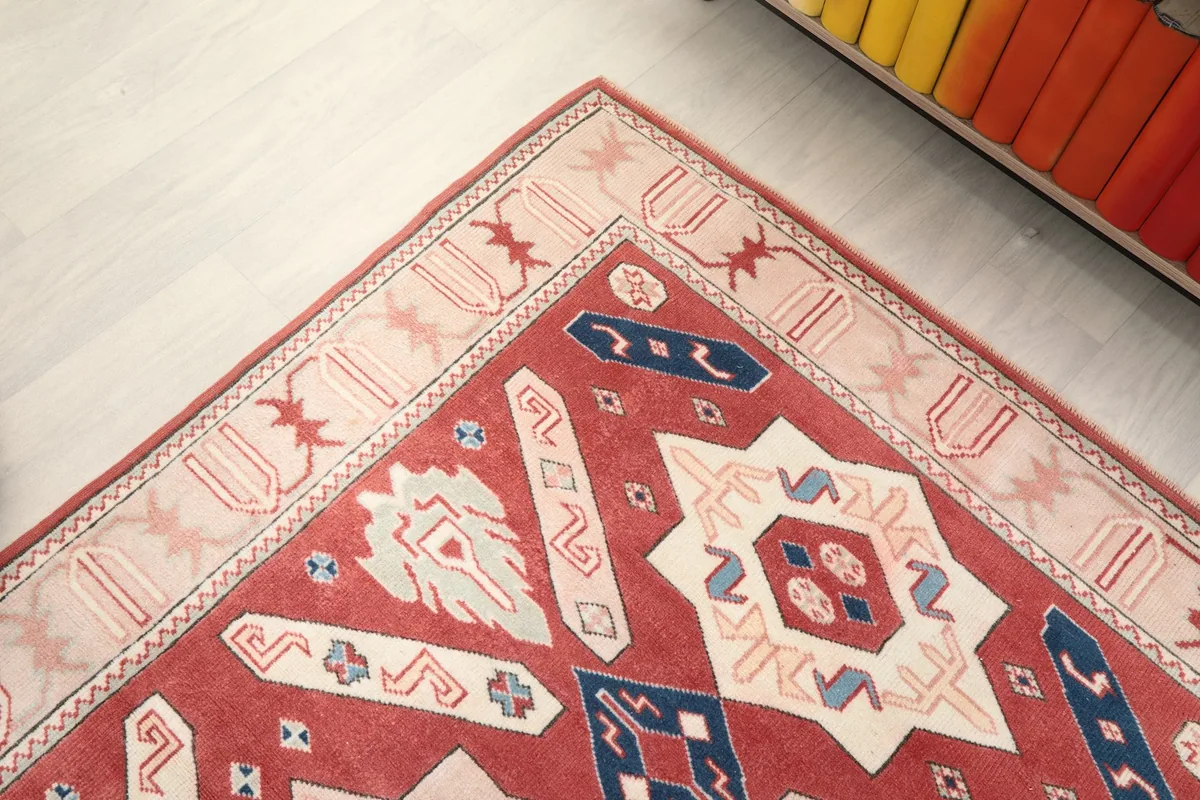 Corner detail of the rug, showing the intricate patterns within the beige border and the red main field.