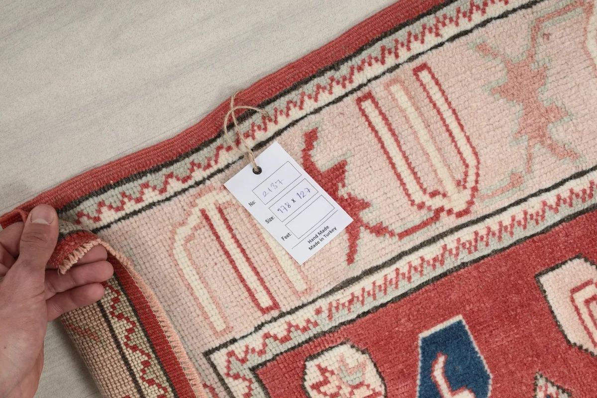 Hand holding the rug's label, showing the size and origin details, against the rug's border.