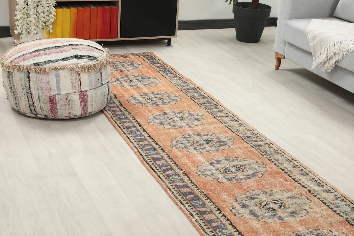 Angled view of the orange runner rug, highlighting its texture and colors next to a striped pouf