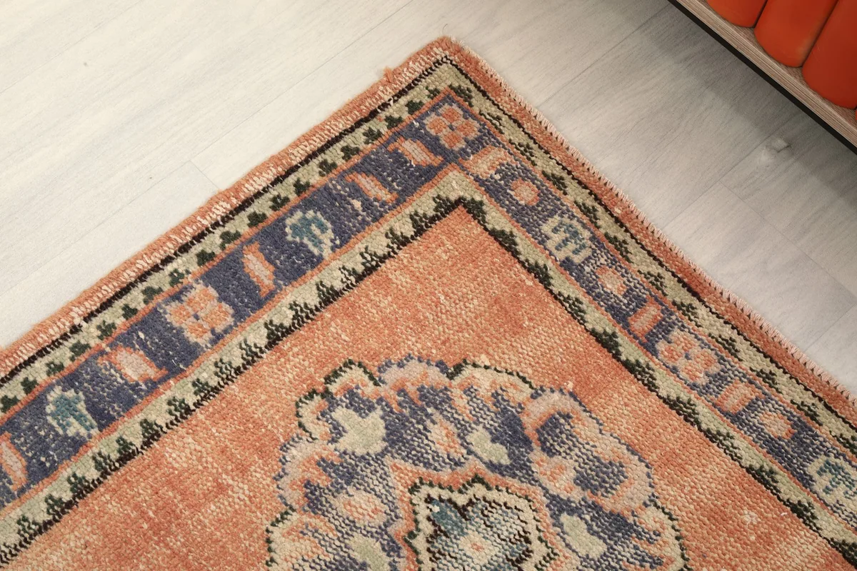 Corner detail of the rug, showing the blend of orange, blue, and beige in the border