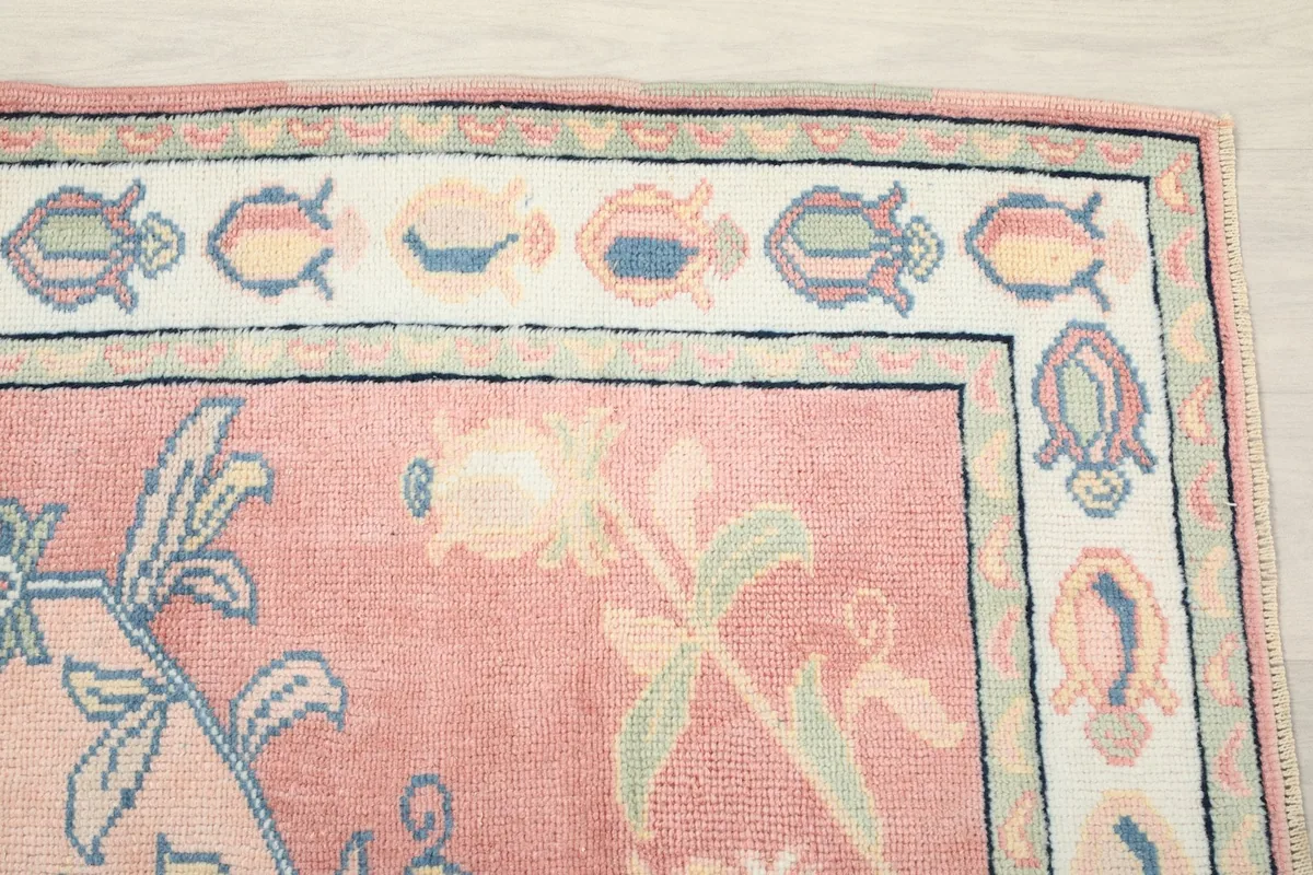 Detail view of the rug's ivory border with multicolored floral motifs and the pink field