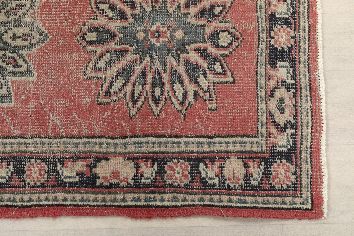 Detailed view of the rug's corner, showing the rose field, navy border, and geometric motifs.