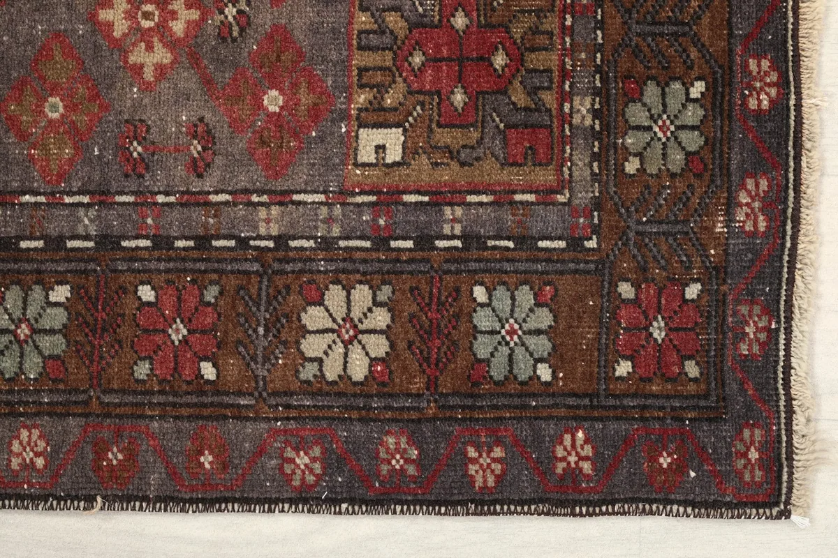 Detailed view of the rug's floral and geometric border patterns in brown and red