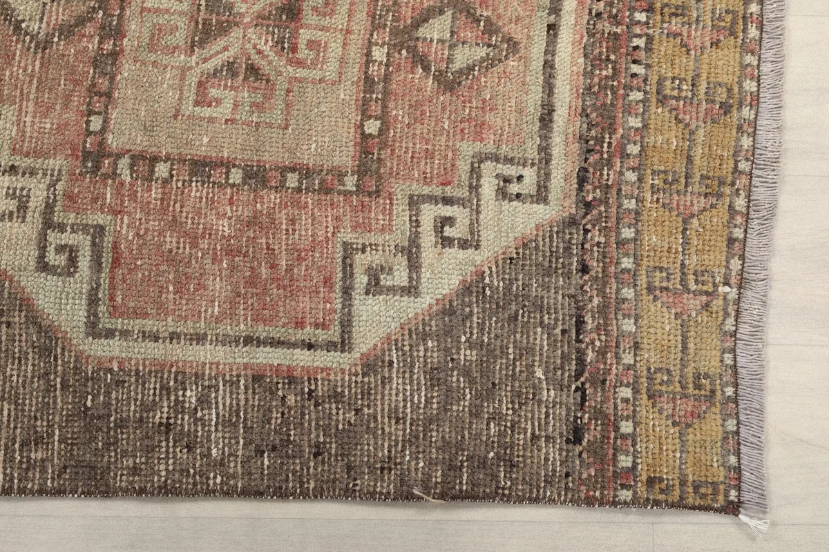Detailed corner view of the rug, showcasing the geometric border and muted rose tones.