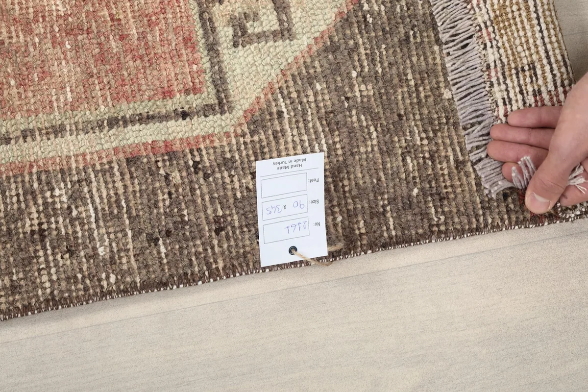 Hand holding a small label near the rug's fringe, showing the quality and finish.