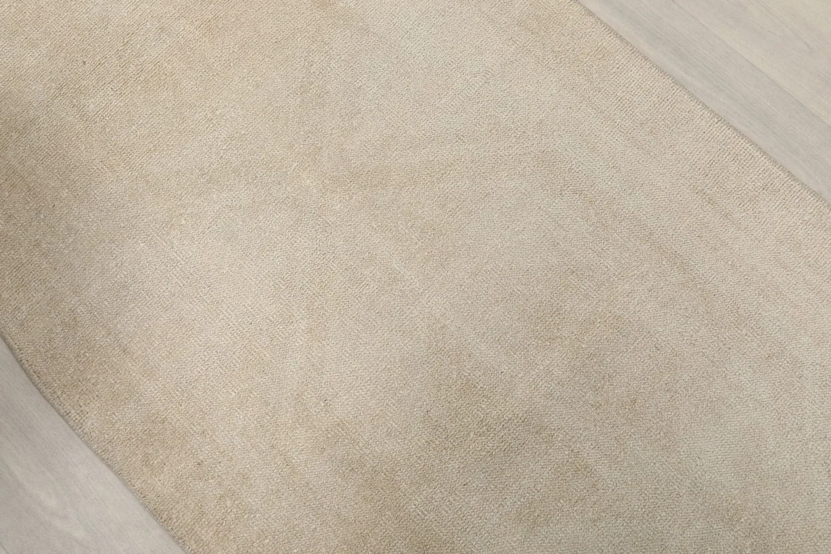 Close-up of the ivory rug's texture, revealing the hand-knotted wool pile and its subtle distressed character.