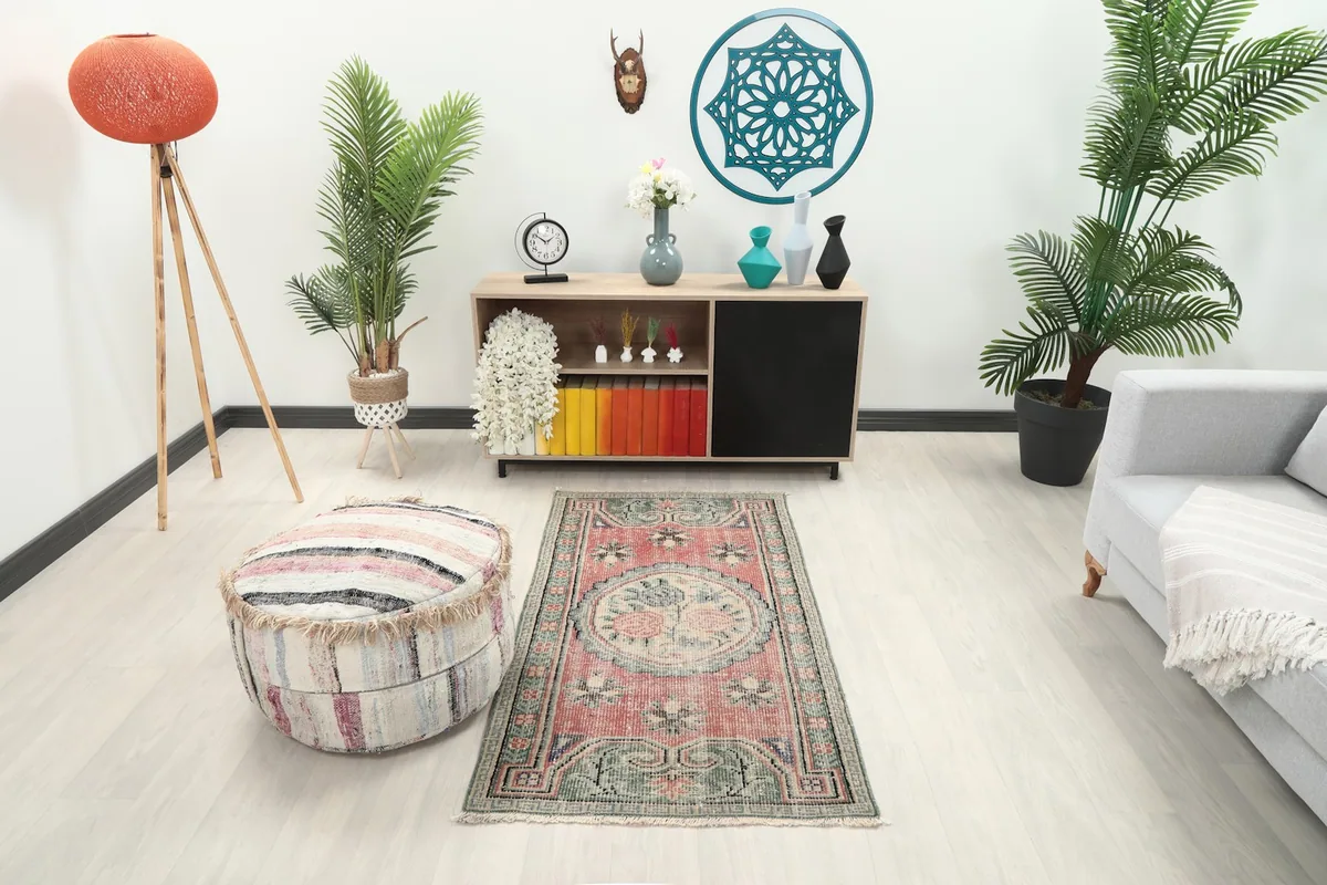 Vintage rose and green rug in a living room setting with a light grey couch and ottoman