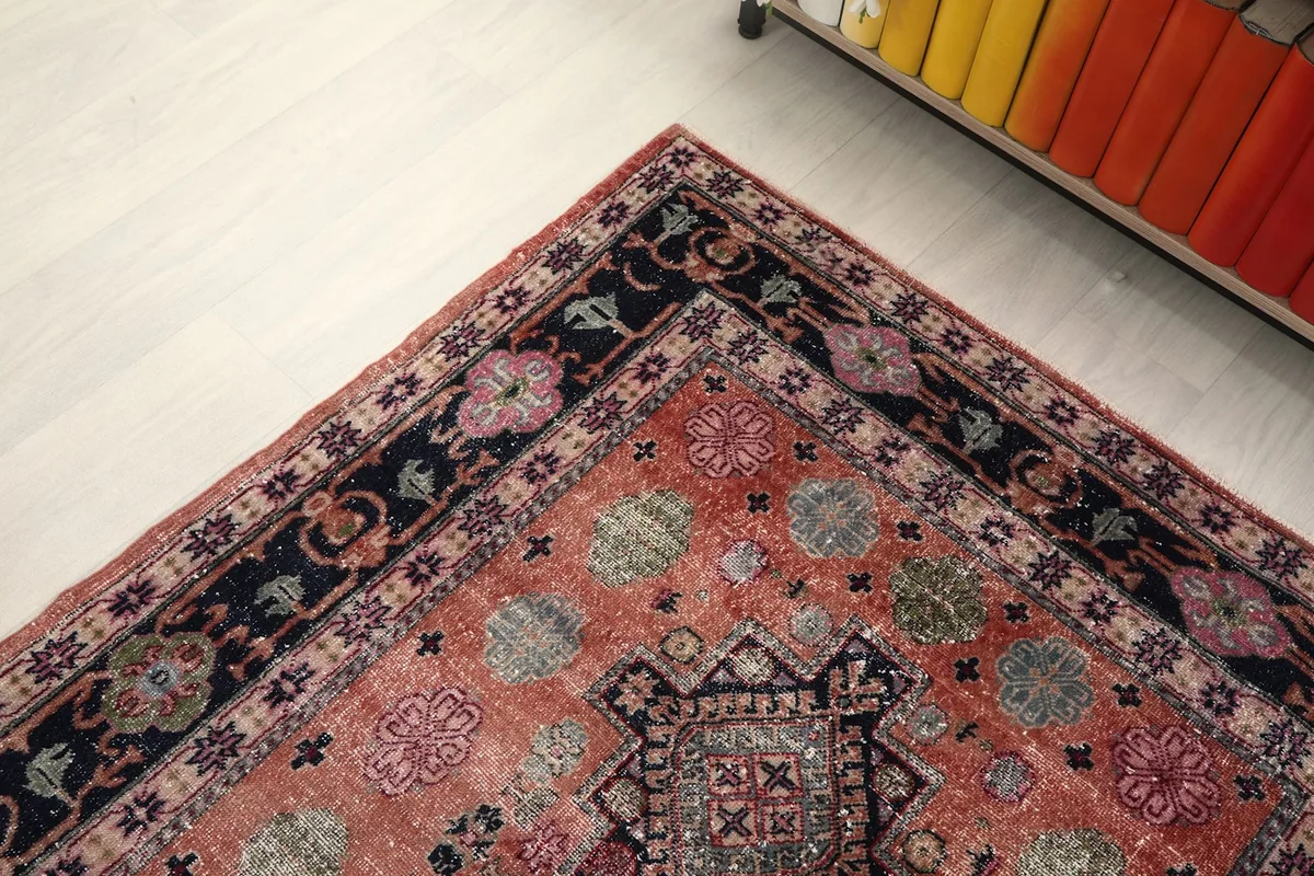 Corner view of the rug, showing the blend of the rust field with the detailed navy and pink border.