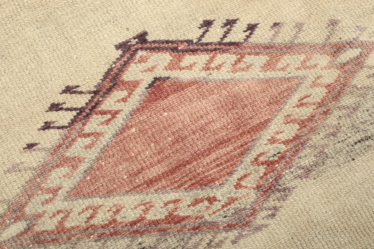 Macro detail of the rust-colored central motif within the beige field, showing individual knots and slight wear.