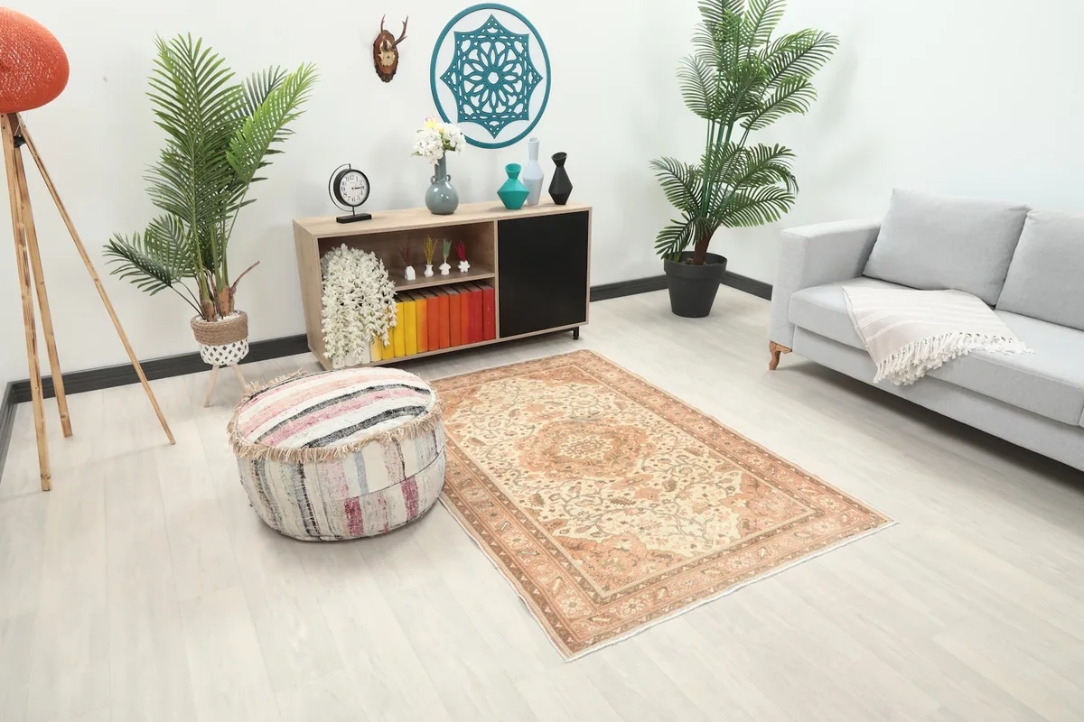 Angled view of the cream and rust rug in a room, showing its placement next to a sofa and ottoman.