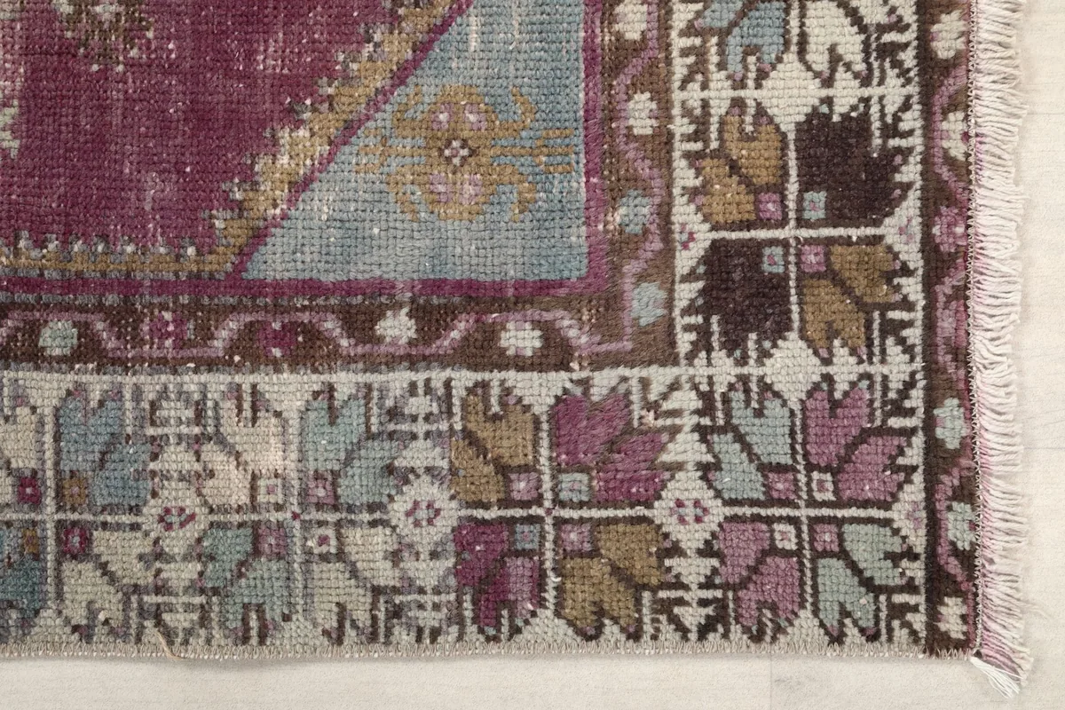 Detailed view of one end of the rug, showing the geometric patterns in rose, blue, and tan