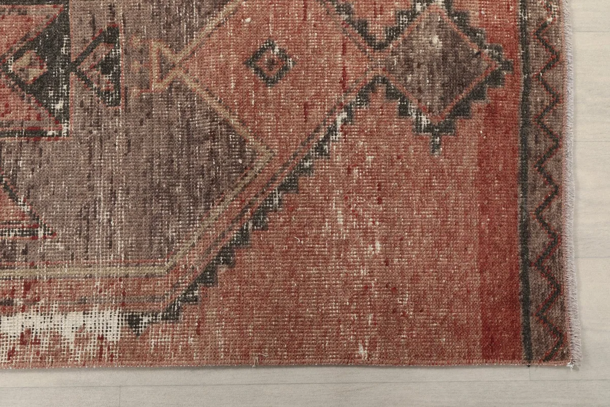 Detailed view of the rug's rust field and charcoal geometric design with visible patina