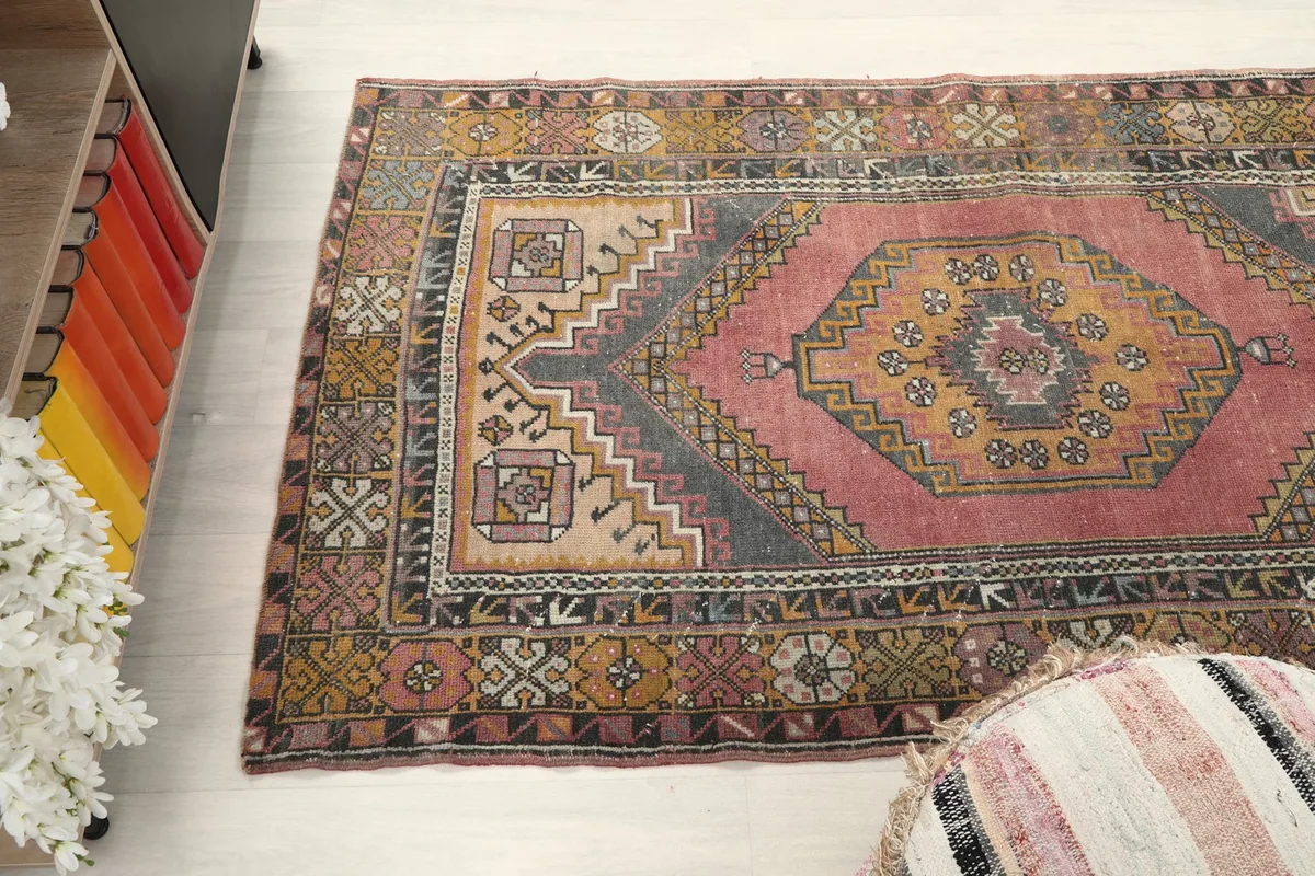 Wide angle view of the rug on the floor, next to a striped pouf and cabinet.