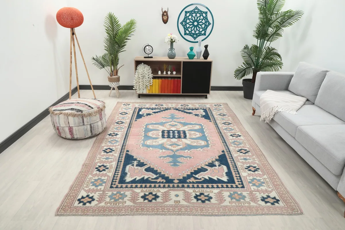 Vintage pink and navy Anatolian rug displayed in a bright living room with a gray sofa and wooden furniture.