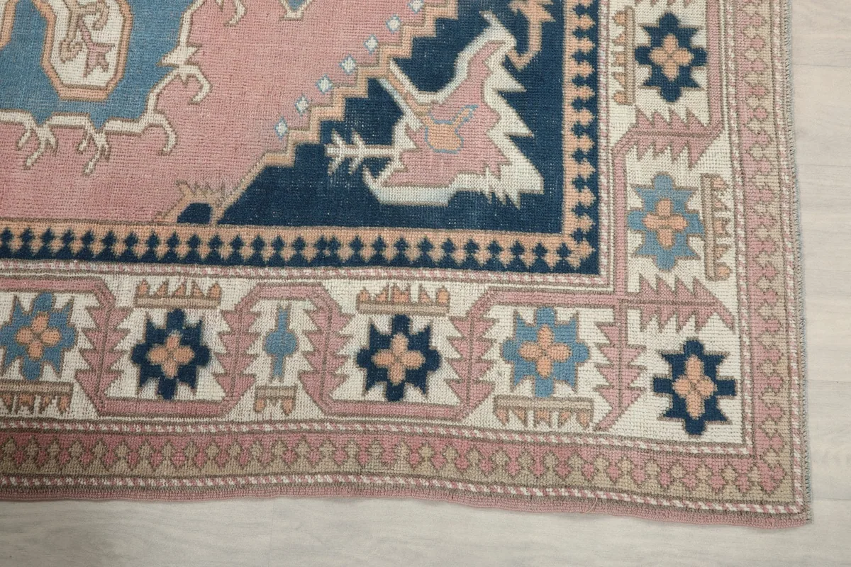 Detailed view of the corner of the rug, showing the pink, navy, and ivory geometric border patterns.