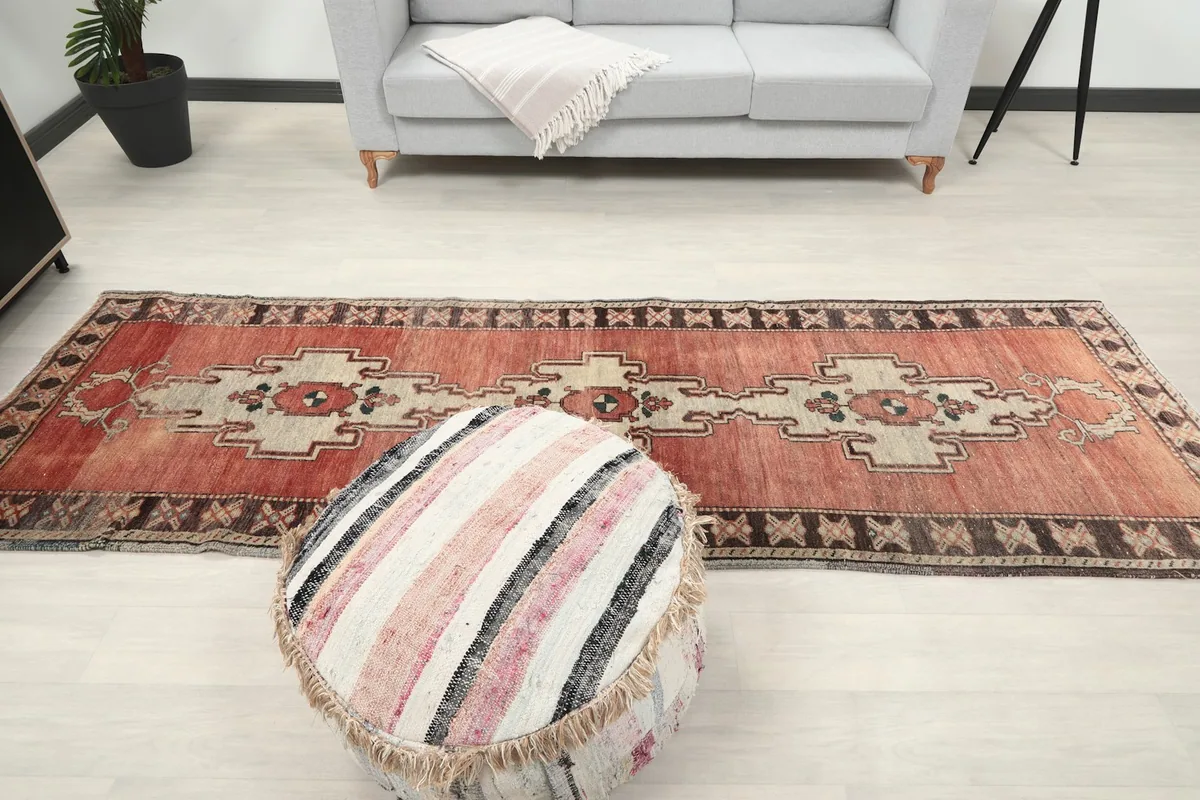 Full view of the runner rug on light flooring with a striped pouf in the foreground