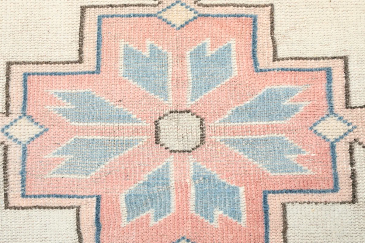 Close-up detail of a rose and blue tribal motif on the rug's ivory background