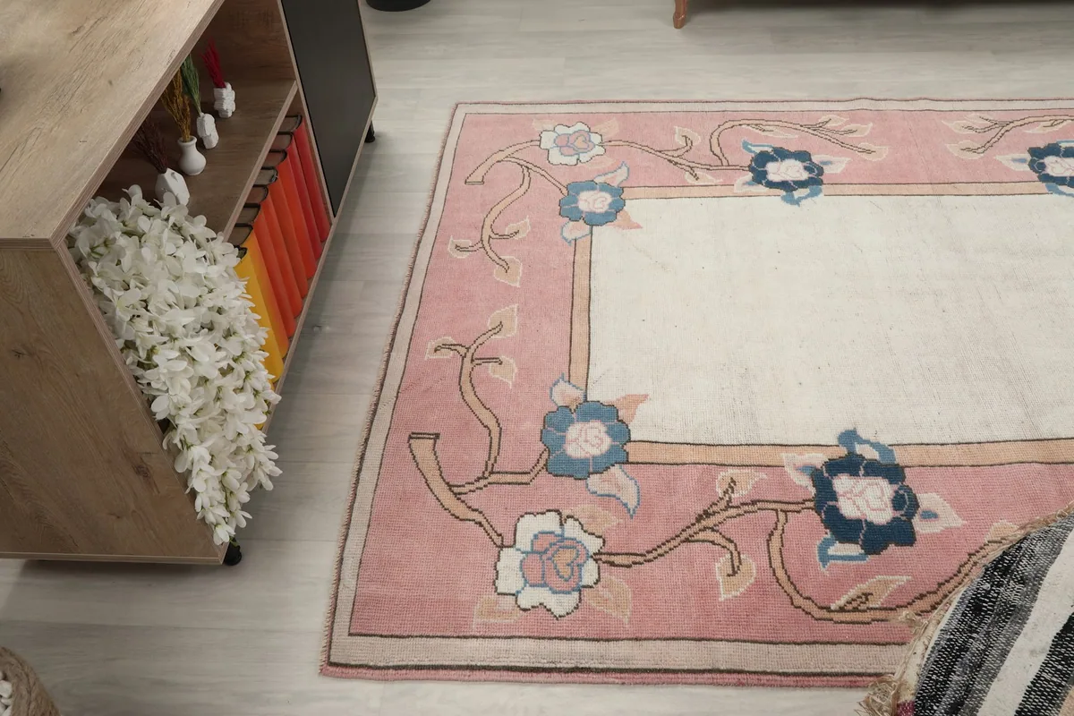 Rug positioned near a wooden cabinet, highlighting the rose border and ivory center