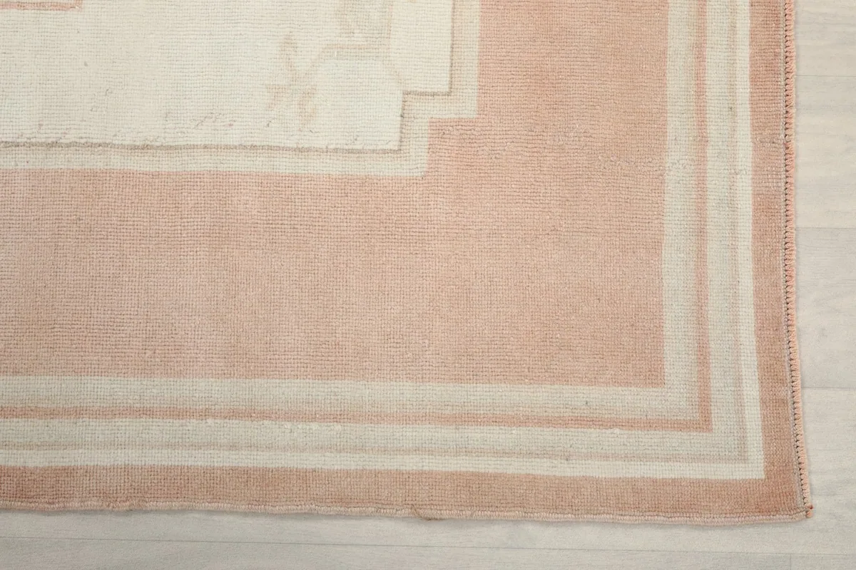 Detail view of the rug's outer pink border and internal ivory lines
