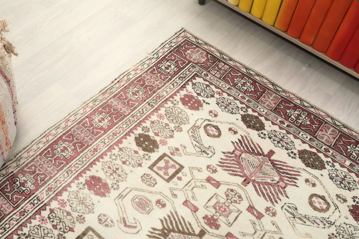 Corner view of the rug, showing the border design and the blend of ivory, rose, and brown hues.