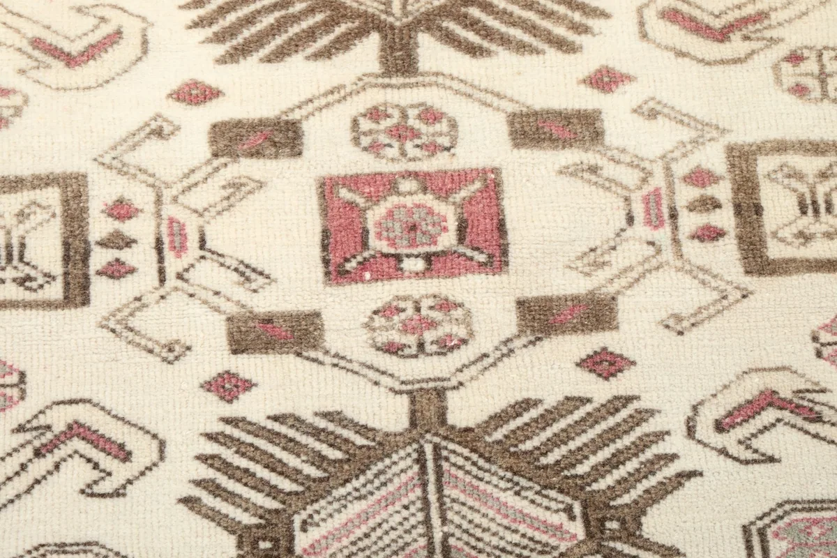 Close-up of a central geometric motif in ivory, rose, and brown, revealing the hand-knotted texture.