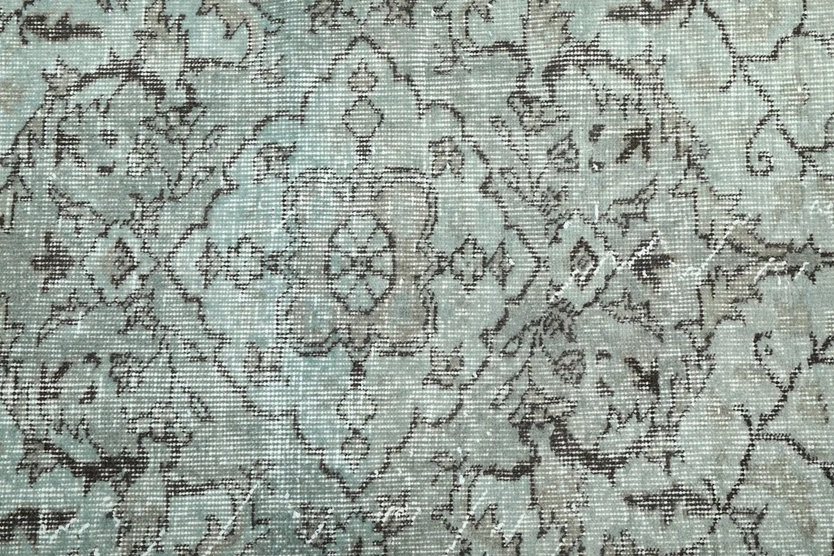 Close-up of the intricate gray geometric and floral motifs against the faded blue field of the rug