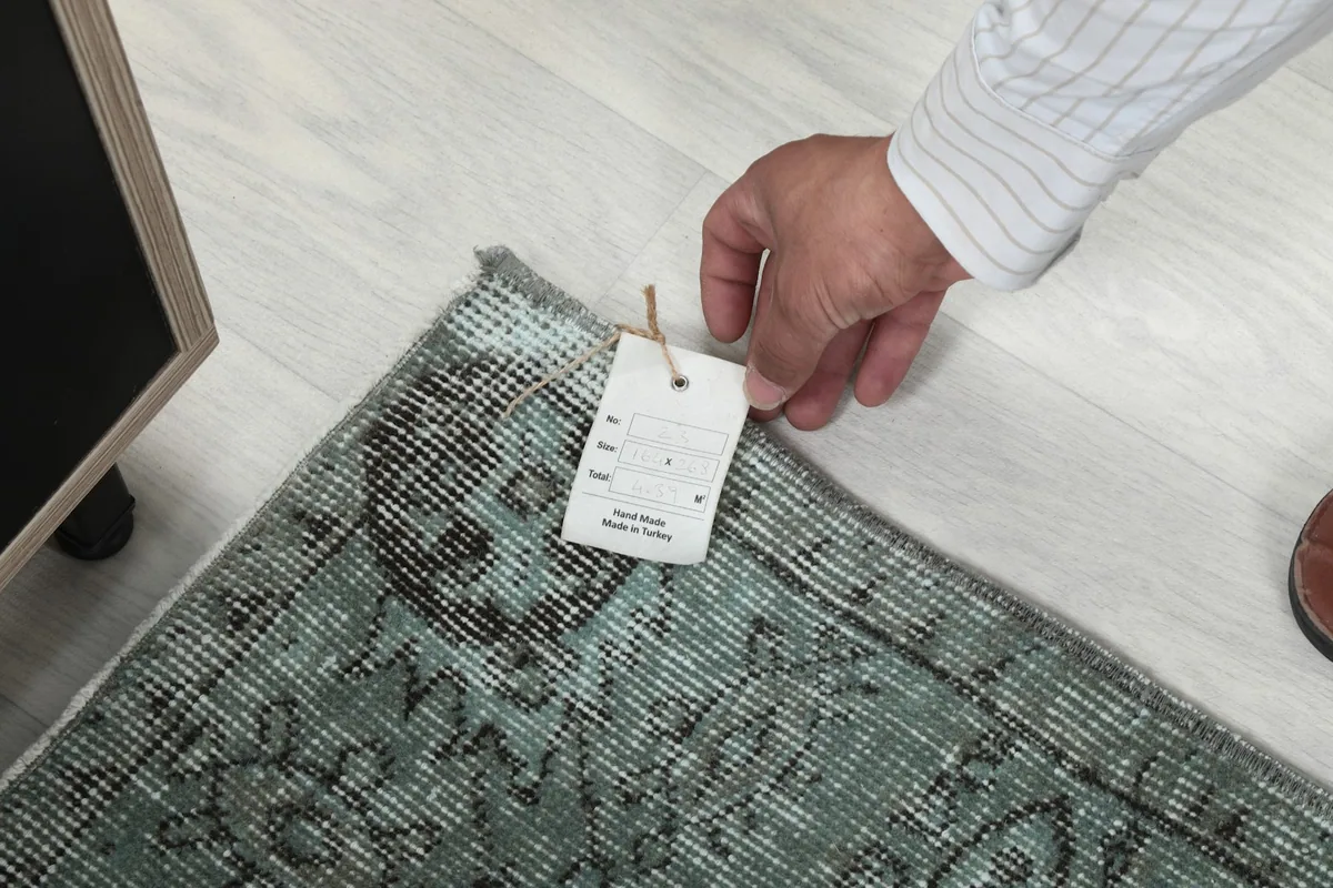 Hand holding a tag on the rug, indicating its origin from Anatolia, Turkey and its vintage nature