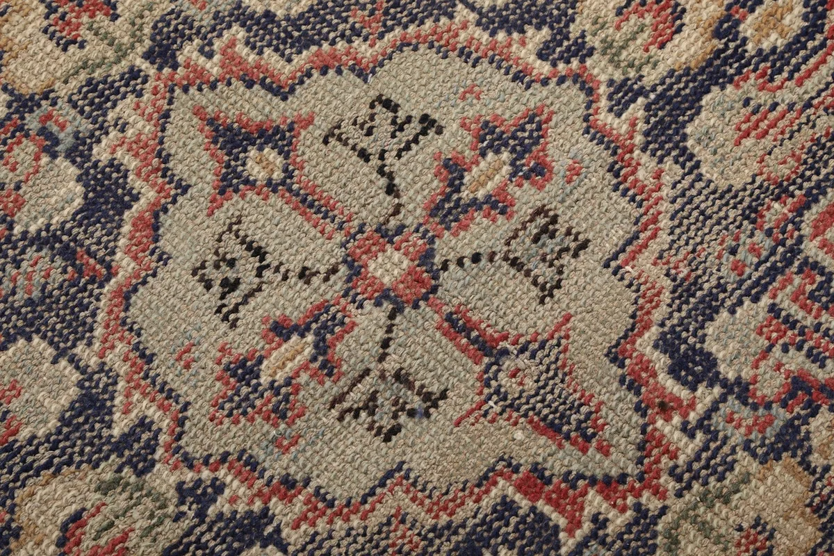 Macro detail of the hand-knotted wool pile, showcasing the intricate navy, red, and beige weaving