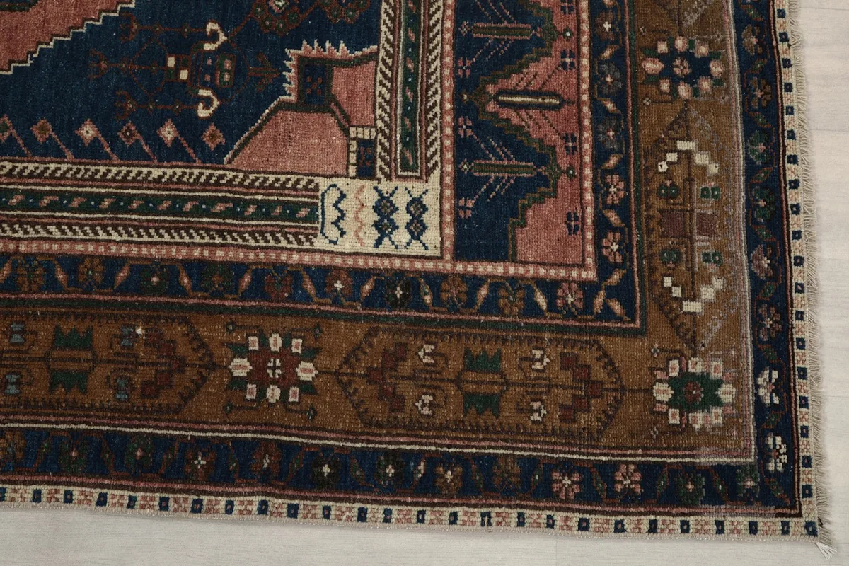 Detail of the brown outer border with subtle geometric motifs and the corner of the rug.