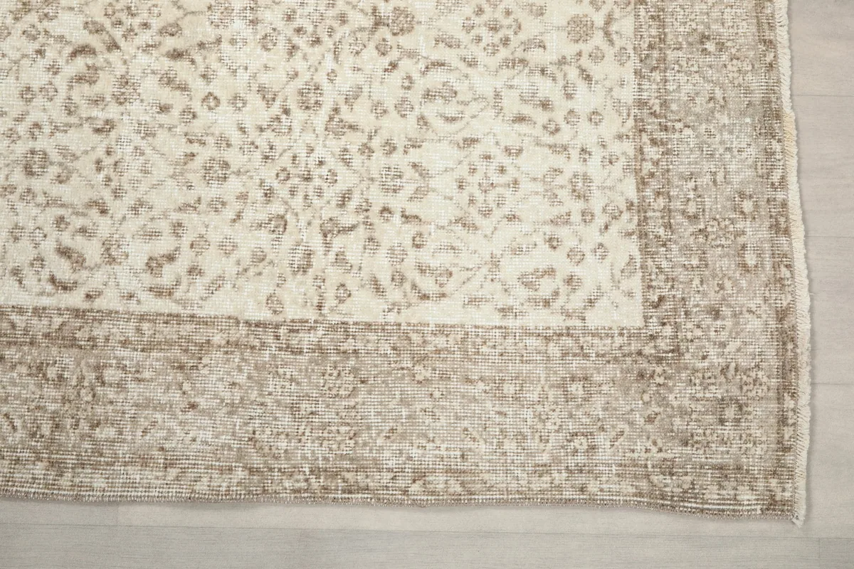 Detailed view of a corner of the rug, highlighting the subtle floral motifs and the worn texture of the border