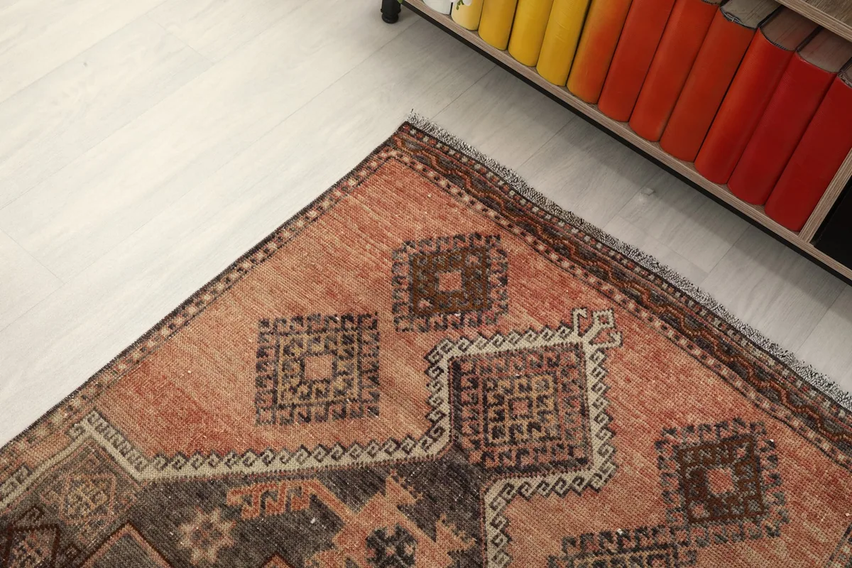Corner angle of the runner rug showing the distressed rust field and brown border next to a cabinet.