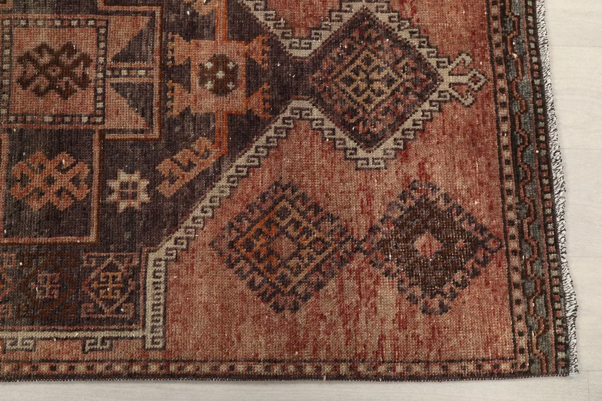Detailed view of the rug's rust field and part of the brown geometric border pattern at one end.