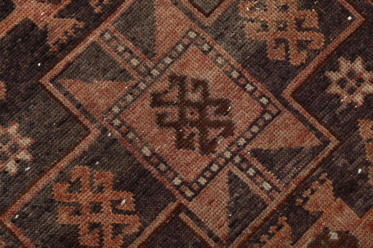 Intricate detail of a central diamond motif with smaller geometric designs within the brown section of the rug.