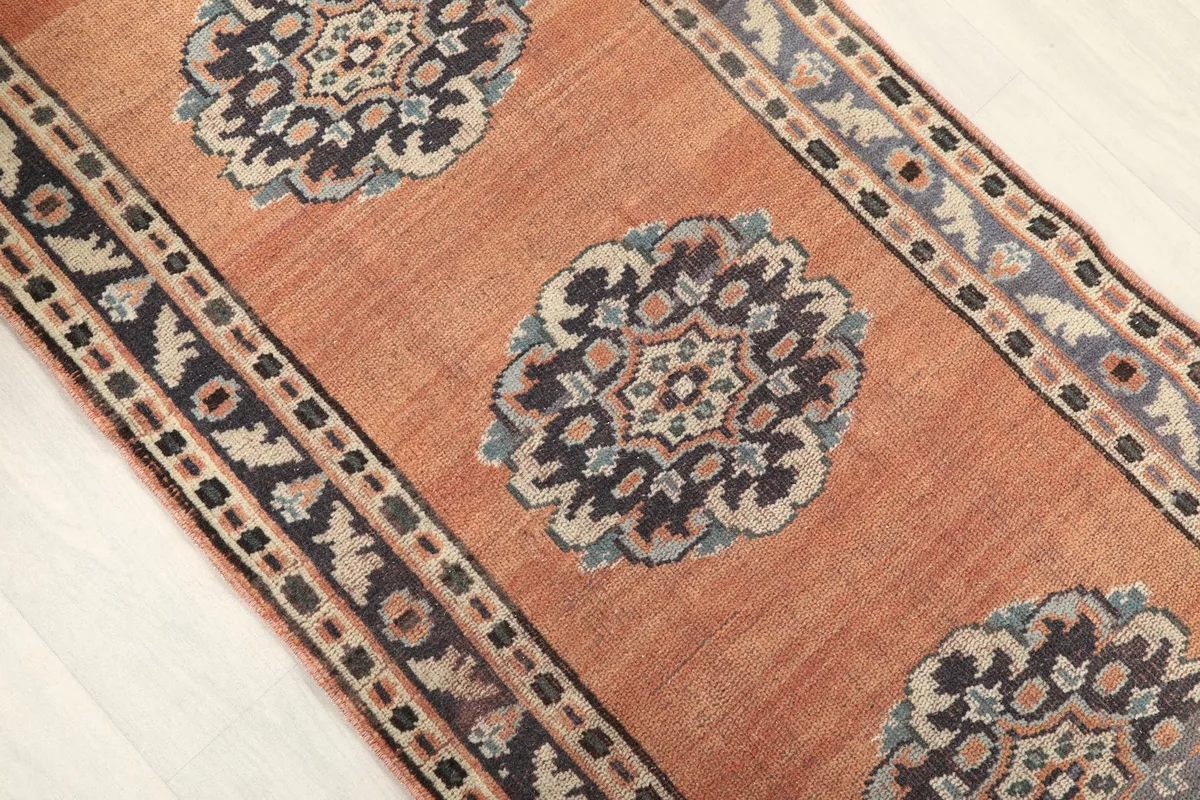Angled view of the rust runner rug, highlighting multiple navy and beige medallions along its length.