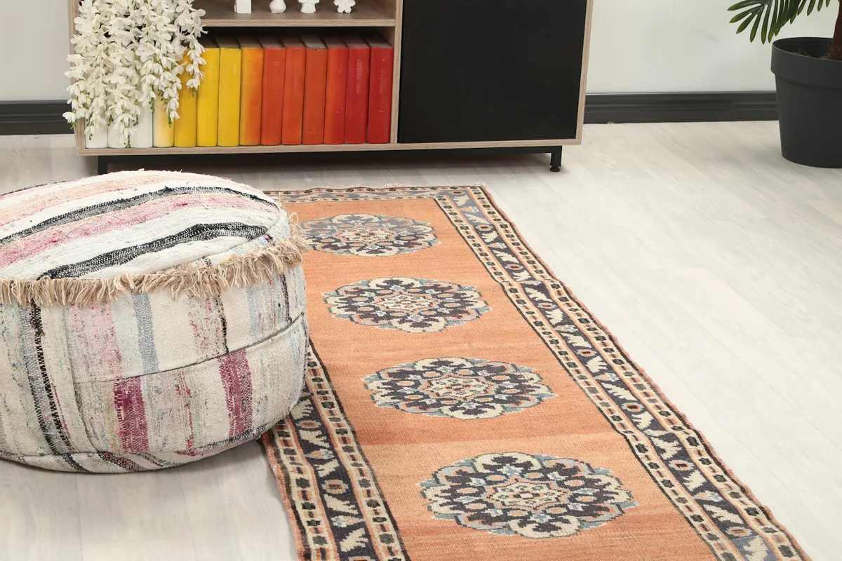 Close-up view of the rust runner rug's medallions and border, with a decorative pouf nearby.