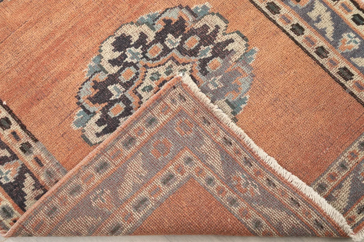 Folded corner of the rust runner rug, revealing the wool pile and cotton foundation.