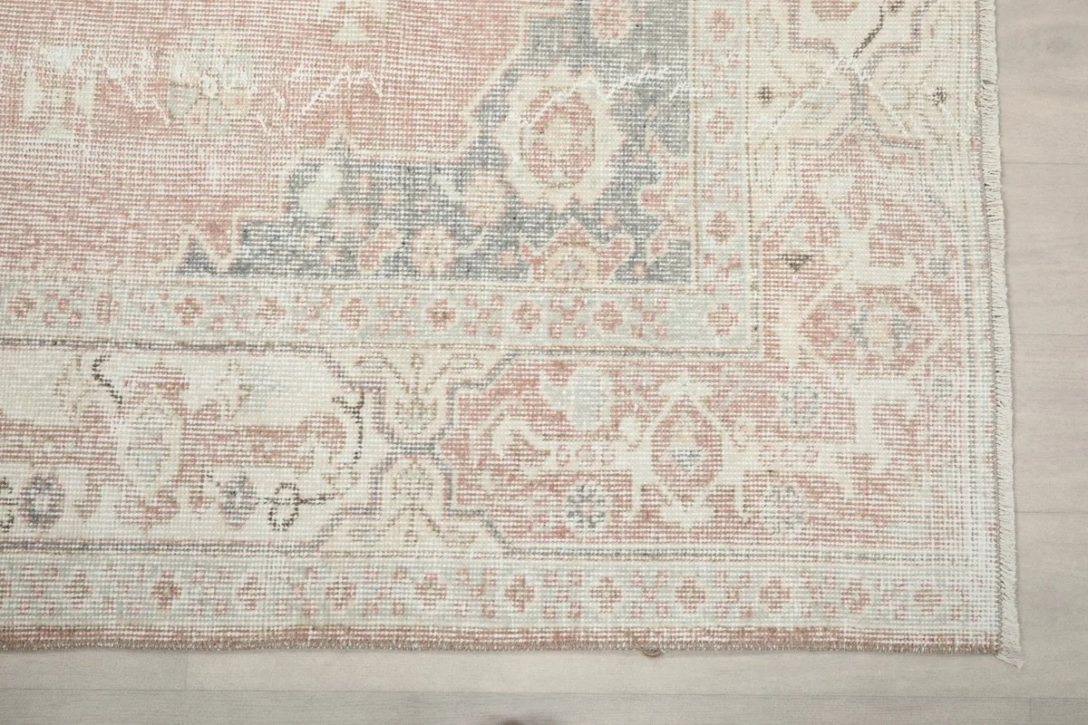 Detail of the rug's outer border, featuring geometric patterns in beige and subtle rose.