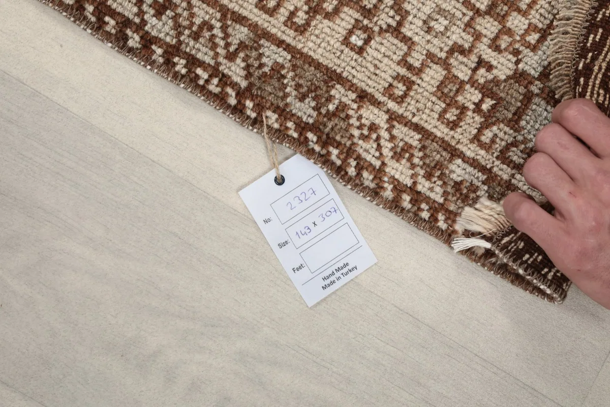 Hand holding a tag with rug details, showing the rug's edge and fringe.