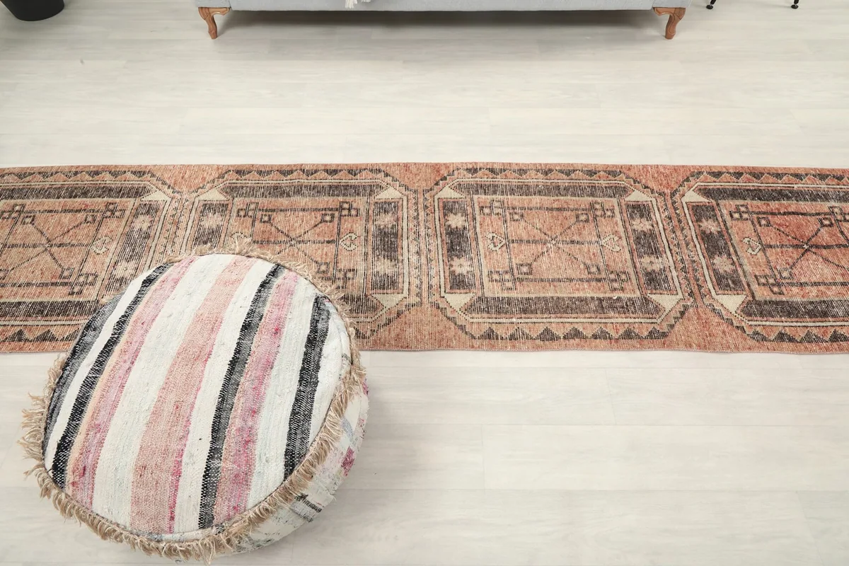 Long view of the runner rug in a room, extending into the background, next to a striped pouf.