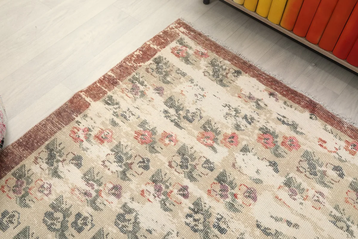 Angled view of the rug, focusing on a section of the beige field and rust border.