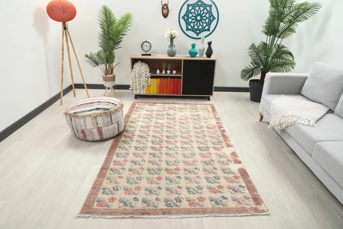 Vintage rug with beige field and floral motifs displayed in a bright room setting.