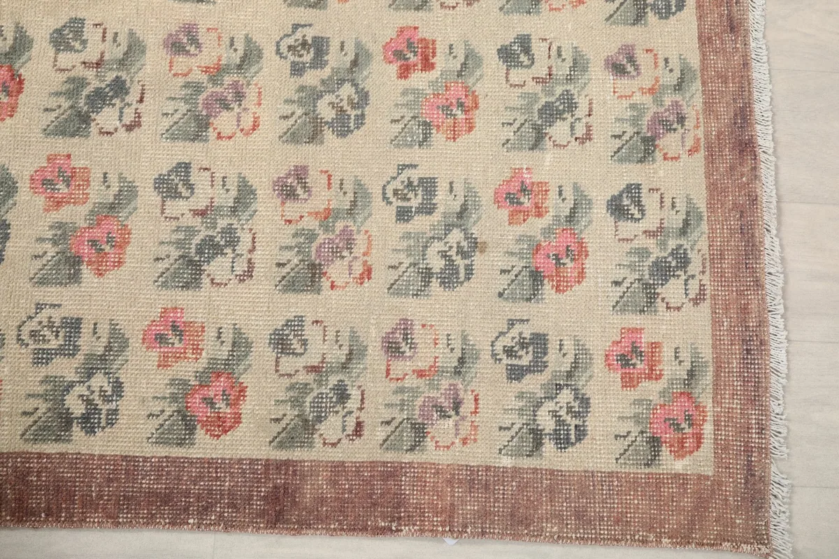 Detailed view of the rug's corner, showing the rust border and beige field with pink and blue flowers.
