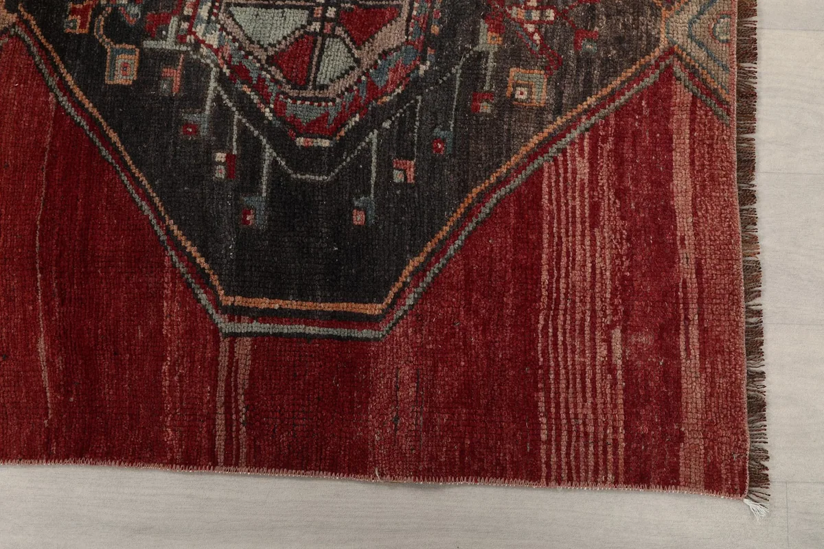 Close-up of the rug's end, showing the rich red field and part of a dark geometric medallion with subtle wear.