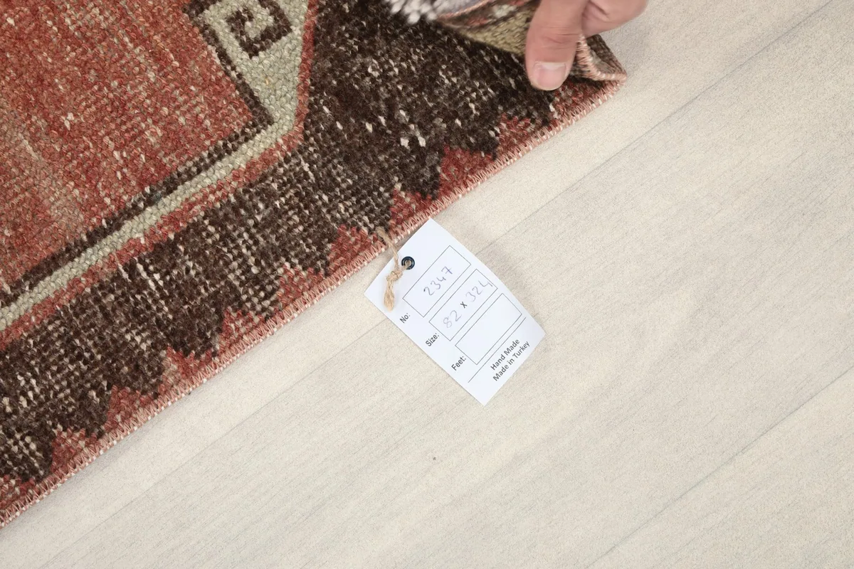 Hand holding a tag with rug dimensions 2'8" x 10'8" (82 x 324 cm) next to the rug