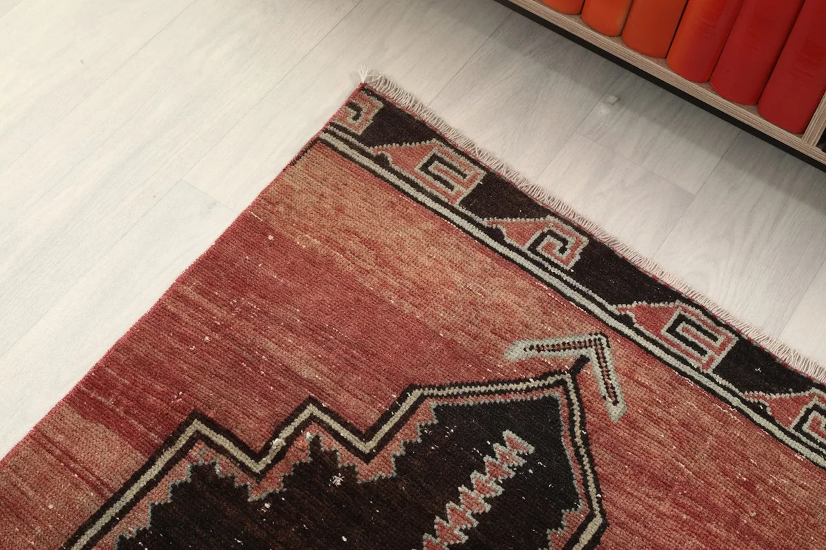 Corner detail of the rug, showing the geometric border pattern and the rust field